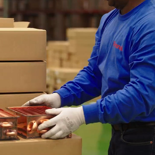 Worker handling water heater part next to cardboard boxes